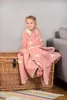 A young girl wrapped in a pink blanket with a horse pattern sits on a wicker chest. Náhľad obrázku produktu