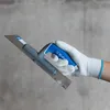 A hand wearing a white glove holds a trowel against a gray concrete wall. Náhled obrázku produktu