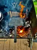 A cast iron waffle maker is being used over an open fire on a grill. Produktbild-Vorschau