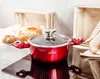 A red pot with a glass lid sits on a black induction stovetop, with bread and wooden crates in the background. Produktbild-Vorschau