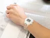 A person's arm wearing a transparent digital watch rests on an open book. Produktbild-Vorschau