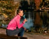A woman is sitting on a bench by a lake, drinking from a water bottle. Anteprima dell’immagine prodotto