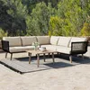 An outdoor patio scene with a sectional sofa and coffee table set on a rug, with trees in the background. Anteprima dell’immagine prodotto