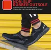 A person wearing black athletic pants with red and white stripes is standing on a metal surface, showcasing a pair of black athletic shoes. The background is a bright yellow corrugated metal wall. Produktbild-Vorschau