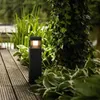 A black bollard light illuminates a garden path next to a tree covered in ivy. Anteprima dell’immagine prodotto