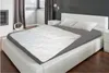 A bedroom scene with a bed made up with a white comforter over a gray sheet. Produktbild-Vorschau