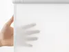 A hand is shown behind a white translucent roller blind. Produktbild-Vorschau