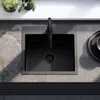 A black kitchen sink with a black faucet is shown from a top-down view, set into a grey stone countertop. Two small potted plants are visible on a white shelf in the background. Produktbild-Vorschau