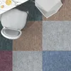 A top-down view of a chair placed on a patchwork carpet with different colored squares. A small table with a drink is visible in the top left corner. Náhled obrázku produktu