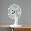 A white table fan is displayed on a wooden surface against a gray wall. Náhľad obrázku produktu