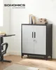 A metal storage cabinet with two doors and a lock, placed in a room with a desk and chair. Produktbild-Vorschau