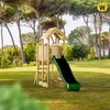 A wooden playground set with a green slide is situated on a grassy lawn, surrounded by tall trees. Náhľad obrázku produktu