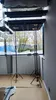 Two adjustable support poles with tripod bases are set up indoors, near a large window overlooking trees. Produktbild-Vorschau