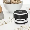 A mini desktop vacuum cleaner is shown on a white surface with crumbs scattered around it. A bowl of bread and an egg in an egg cup are in the background. Anteprima dell’immagine prodotto