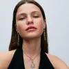 A close-up shot of a woman wearing a necklace and earrings. Anteprima dell’immagine prodotto
