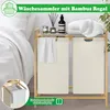 A laundry basket with a bamboo shelf is shown next to a bed, with towels and decorative items on the shelf. Produktbild-Vorschau