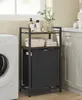 A laundry cart with a hamper and shelves is placed next to a washing machine in a laundry room. Produktbild-Vorschau