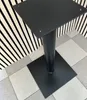 A black metal table base with a square top and a square base is shown on a tiled floor in front of a wall with black and white striped paneling. Náhled obrázku produktu