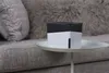 A small black and white device sits on a small round table next to a couch. Produktbild-Vorschau