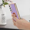A hand holding a purple phone case with a gold trim and a ring holder, next to a vase with flowers. Produktbild-Vorschau