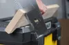 A person is using a hand saw to cut a piece of wood that is resting on a black and yellow toolbox. Voir les images du produit