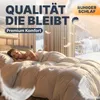 A woman sleeping peacefully under a fluffy duvet in a cozy bedroom with a winter view outside the window. Produktbild-Vorschau
