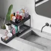 Schwarzer zweistufiger Schiebe-Organizer gefüllt mit verschiedenen Toilettenartikeln und Kosmetika auf einer grauen Badezimmerablage neben einem Waschbecken Anteprima dell’immagine prodotto