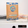 A product shot of OceanWash Waschmittelblätter on a counter, with folded laundry in the background. Produktbild-Vorschau