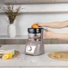 A person is using a kitchen machine to juice an orange in a kitchen setting. Produktbild-Vorschau