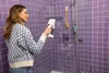 A woman is cleaning a shower with a Kärcher WV 1 electric window cleaner. Voir les images du produit