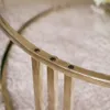A close-up view of the edge of a round coffee table with gold-colored metal legs and a gold-colored rim, showing several black screws. Produktbild-Vorschau