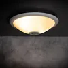 A ceiling light fixture with a motion sensor is mounted on a dark ceiling above a textured gray wall. Produktbild-Vorschau