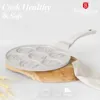 A cream-colored pancake pan with multiple character molds is placed on a wooden board, with wheat stalks in the foreground and text overlays at the top and bottom. Voir les images du produit