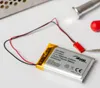 A lithium polymer battery with wires and a connector is shown on a white surface, with tools in the background. Produktbild-Vorschau