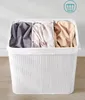 A white, three-compartment laundry basket made of bamboo, filled with folded laundry in shades of gray, beige, and light pink. Produktbild-Vorschau