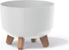 A white planter pot with three brown wooden legs, shown against a white background. Náhľad obrázku produktu