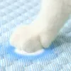 A close-up of a white cat's paw resting on a blue and white striped cooling mat. Náhľad obrázku produktu