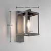 A modern gray outdoor wall lamp with a clear glass cylinder and a visible light bulb, mounted on a light gray wall. Dimensions are indicated with measurement lines. Anteprima dell’immagine prodotto
