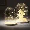 Two glass domes with fairy lights and decorative elements inside, placed on wooden bases. Produktbild-Vorschau