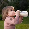 A young child drinking from a baby bottle outdoors. Anteprima dell’immagine prodotto