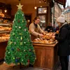 A Christmas tree decorated with ornaments stands in front of a bakery counter where a baker is serving a customer. Voir les images du produit