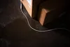 A close-up view of a white cable lying on a dark, wet floor next to cardboard boxes. Podgląd zdjęcia produktu