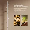 A white towel warmer with a tree-like design is shown on a light brown wall. Two smaller inset images show a bird silhouette on a branch and a hand holding a seedling. Produktbild-Vorschau