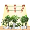 Several potted plants are arranged on a wooden surface, illuminated by three overhead LED grow lights. Produktbild-Vorschau