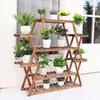 A wooden plant stand filled with various potted plants, placed outdoors near a window. Anteprima dell’immagine prodotto