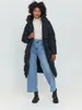 A woman wearing a black puffer coat and blue jeans stands against a white background. Produktbild-Vorschau