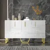 A white sideboard with gold accents is displayed in a modern room with a marble-patterned wall. Produktbild-Vorschau
