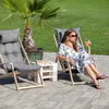 A woman relaxing in a lounge chair outdoors next to a palm tree, with a small table between two chairs. Produktbild-Vorschau