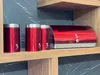 A red bread bin and three matching storage containers are displayed on a wooden shelf against a dark marble-patterned background. Náhled obrázku produktu