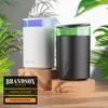 Two aroma diffusers, one white and one black, are displayed on wooden pedestals surrounded by lush green foliage, with dappled sunlight creating shadows. Produktbild-Vorschau